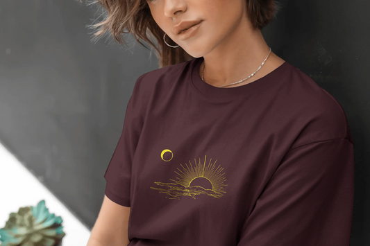 Person wearing a maroon t-shirt with a gold graphic design against a dark background