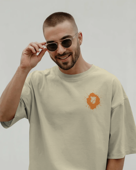 Man wearing a beige t-shirt with a logo, adjusting sunglasses against a plain background