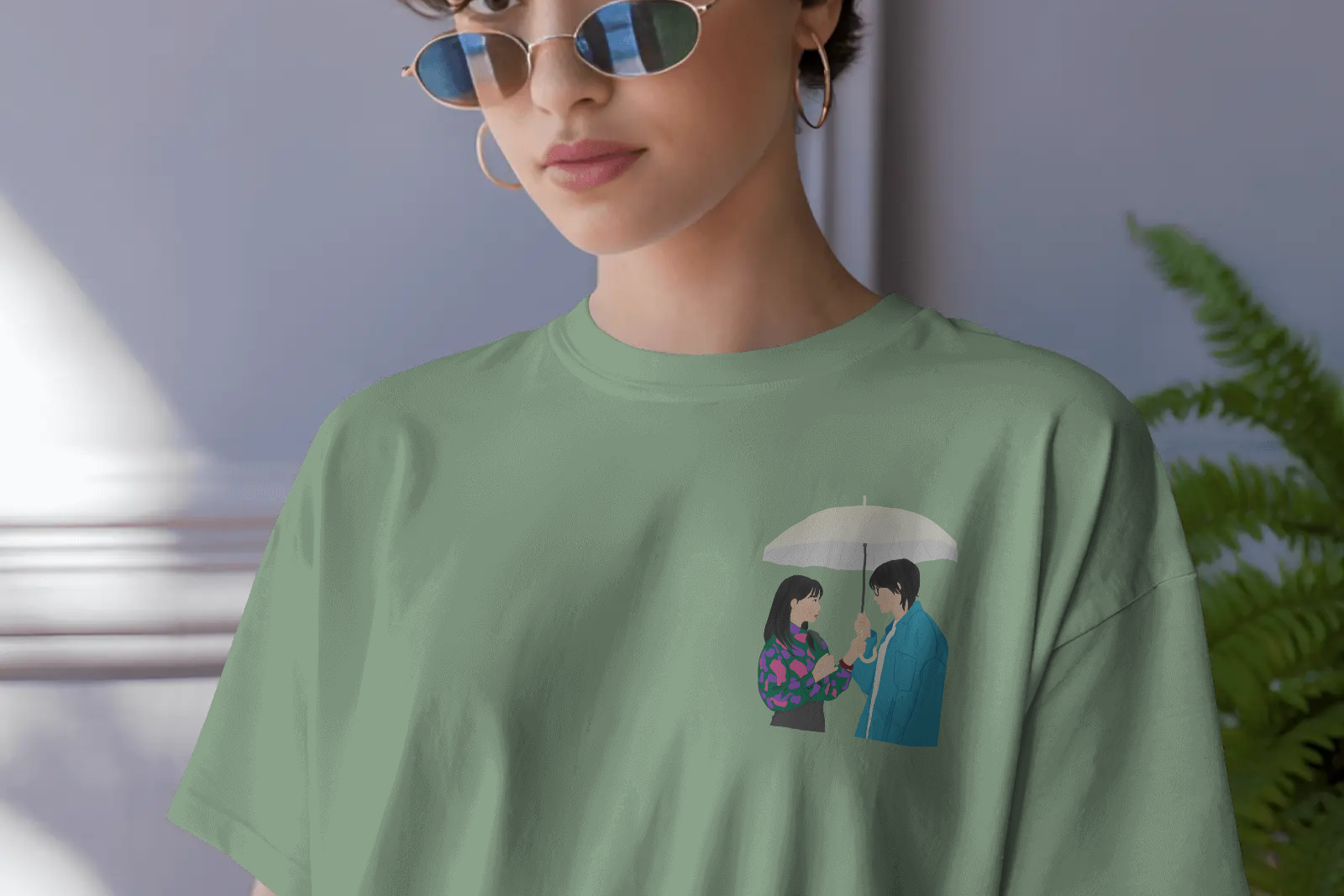 Women wearing a green t-shirt with a graphic design, standing indoors with a neutral background.