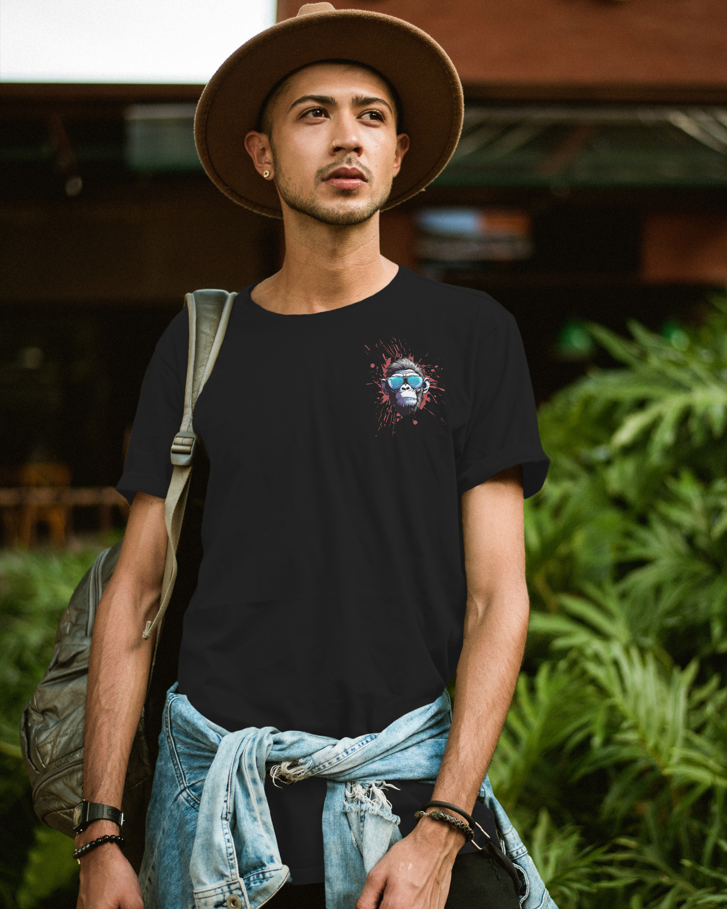 Man wearing a black t-shirt with a graphic design, standing outdoors with greenery in the background.