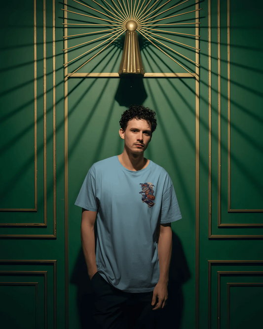 Person wearing a light blue t-shirt with a design against a green wall with gold accents