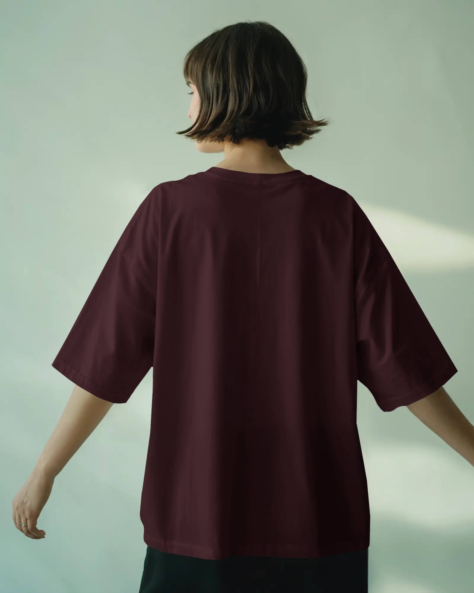 Person wearing a burgundy oversized t-shirt against a light green background