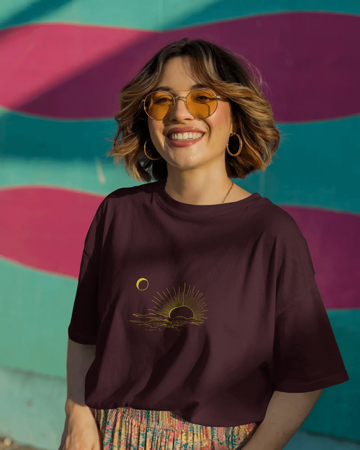 Woman wearing a dark purple t-shirt with a sun and moon design against a colorful striped wall.