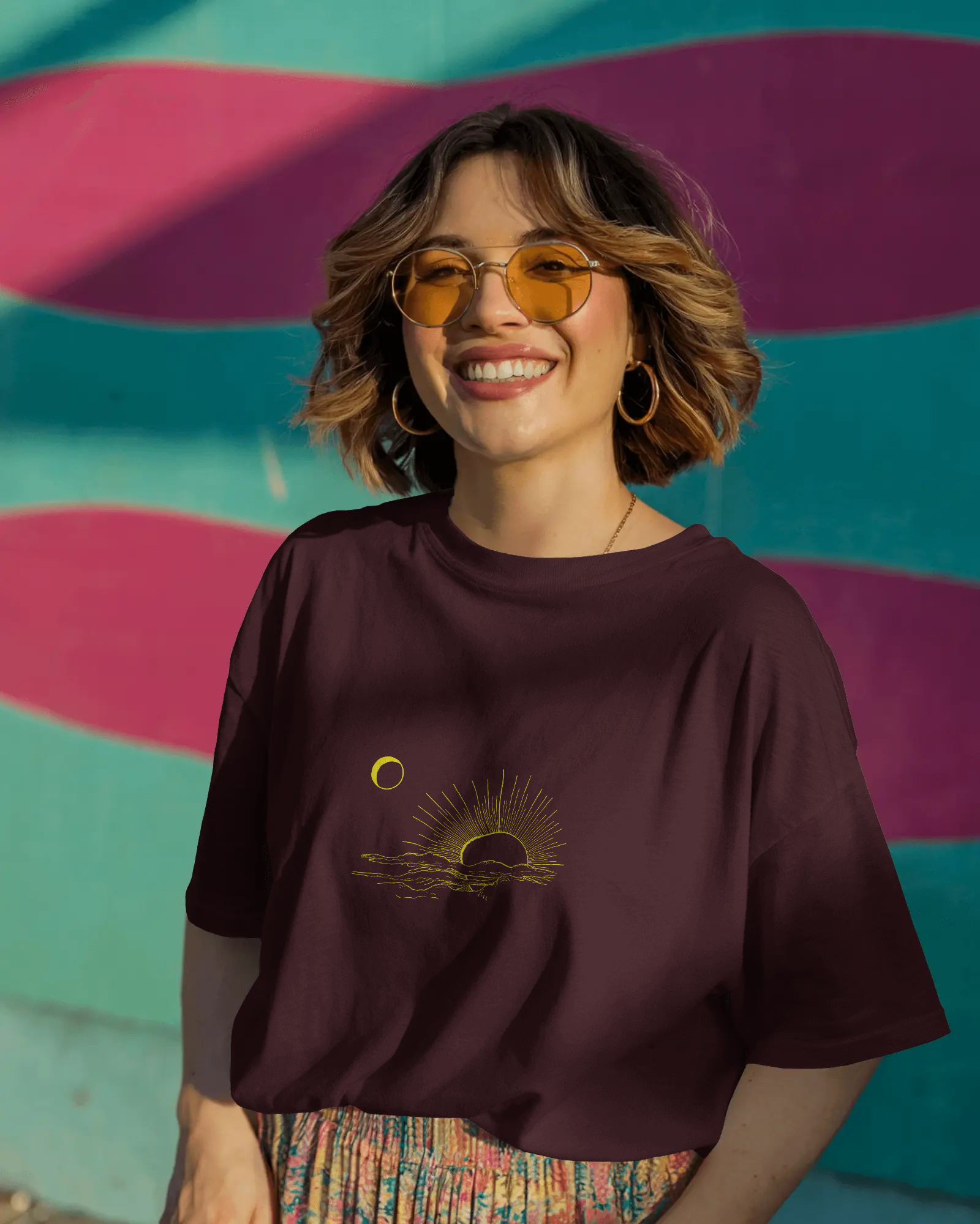 Woman wearing a dark purple t-shirt with a sun and moon design against a colorful striped wall.