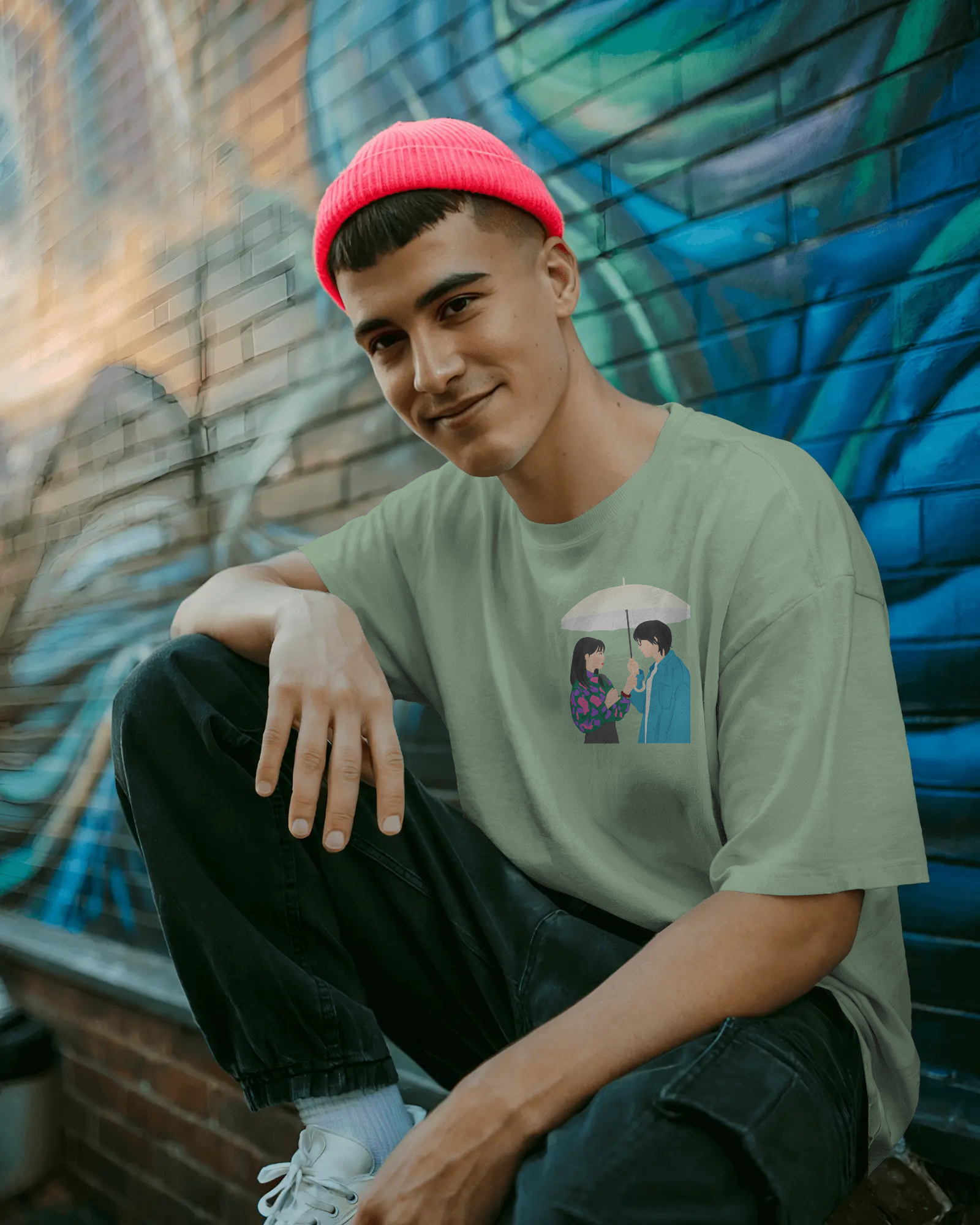 Person wearing a green t-shirt with a graphic design, sitting against a colorful mural.